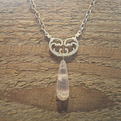 Zilver 925 ankerketting met een symmetrische tussenhanger met krulwerk en op het balanspunt een ophanging met een unieke druppelvormige rozenkwarts. Handgemaakt ontwerp door Goudsmederij Goedbloed